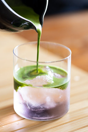 A glass of fresh matcha drink with coconut water presented in multiple layers with rock ice on wooden table.の写真素材