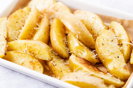 Potato wedges in white baking tray with parmesan cheese and pepper. Homemade cooking concept.の写真素材