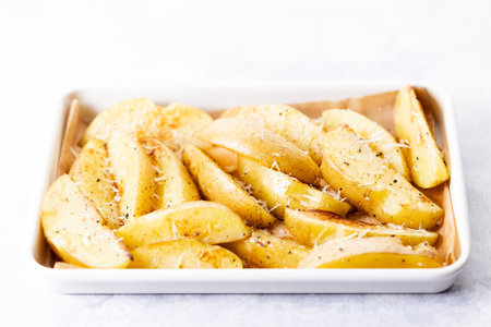 Potato wedges in white baking tray with parmesan cheese and pepper. Homemade cooking concept.の写真素材