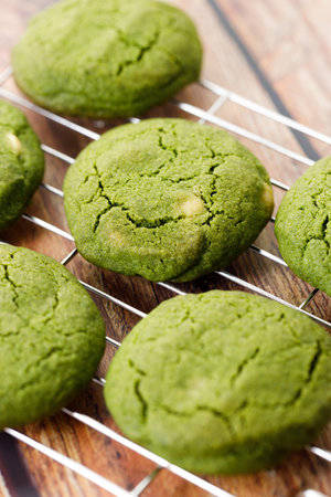 Green tea matcha cookies with white chocolate chips on cooling rack on wooden table. Freshly baked pastries with green tea. Closeup.の写真素材
