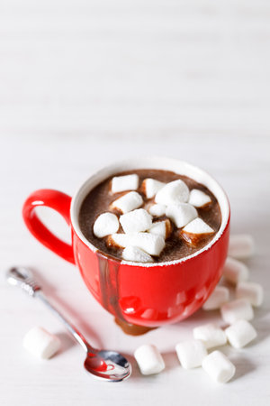 Hot chocolate in red cup with white small marshmallows on white wooden table background.の写真素材
