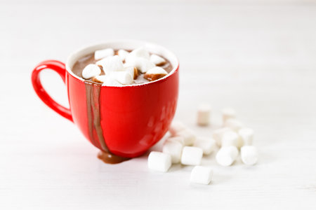 Hot chocolate in red cup with white small marshmallows on white wooden table background.の写真素材