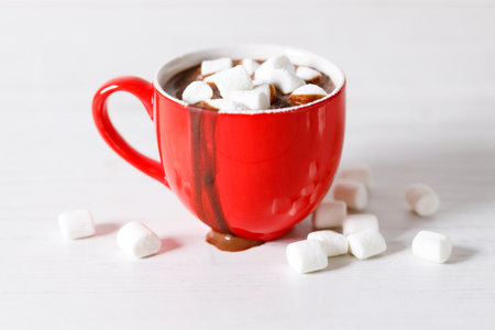 Hot chocolate in red cup with white small marshmallows on white wooden table background.の写真素材
