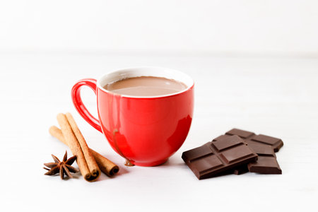 Hot chocolate in red cup with chocolate and spices on white wooden table background.の写真素材