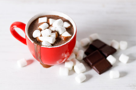 Hot chocolate in red cup with white small marshmallows on white wooden table background.の写真素材