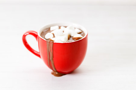 Hot chocolate in red cup with white small marshmallows on white wooden table background.の写真素材