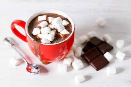 Hot chocolate in red cup with white small marshmallows on white wooden table background.の写真素材