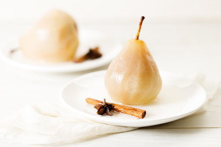 Delicious poached pears on white plate with cinnamon stick and star anise. Delicious and easy dessert.の写真素材