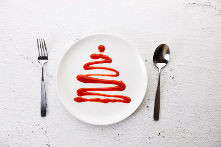 White plate with tomato sauce in Christmas tree shape on white wooden background. Christmas party concept.の写真素材