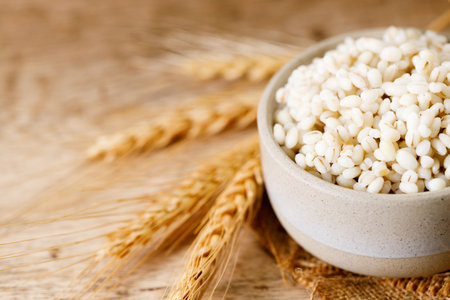 Close up of cooked barley grains and beardless wheat ears on wooden table.の写真素材