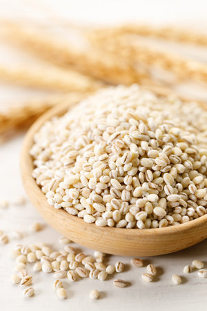 Barley grains in wooden cup on white wooden table. Closeup of barley rice healthy food.の写真素材