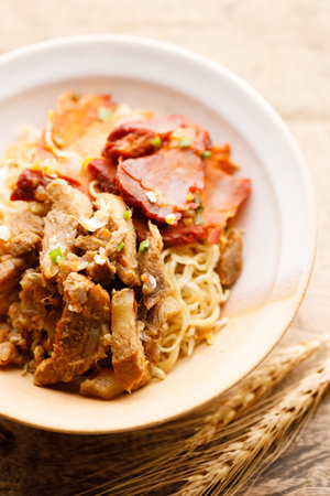 Egg Noodles with sweet pork toppings in a ceramic bowl. Egg Noodles with meat on wooden table. Chinese Food fusion style.の写真素材