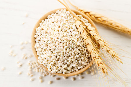Barley grains in wooden cup on white wooden table. Closeup of barley rice healthy food.の写真素材