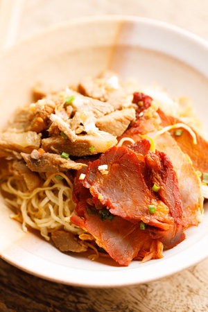 Egg Noodles with sweet pork toppings in a ceramic bowl. Egg Noodles with meat on wooden table. Chinese Food fusion style.の写真素材