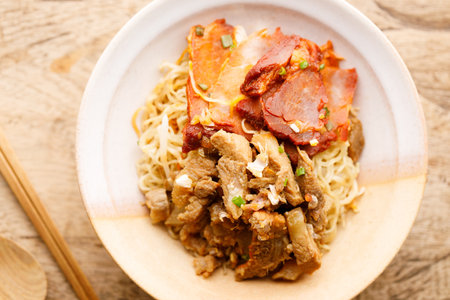 Egg Noodles with sweet pork toppings in a ceramic bowl. Egg Noodles with meat on wooden table. Chinese Food fusion style.の写真素材