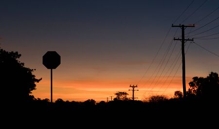 Stop sign and power lines in silhouette at sunsetの写真素材