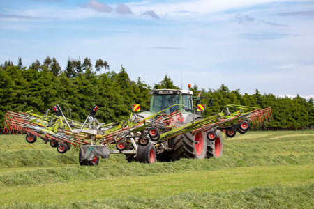 Canterbury, New Zealand - November 17 2018: A green Fendt tractor and tedder working in a farm field raking cut grass into rows for the hay balerのeditorial素材