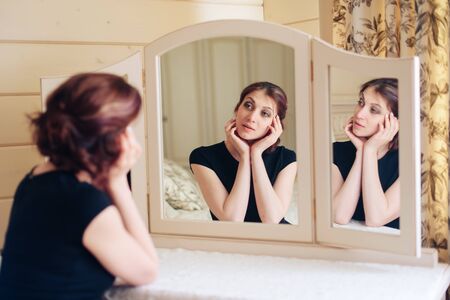 Beautiful young girl in a black dress sits in front of a vintage mirror, reflected in three mirrors 1の写真素材