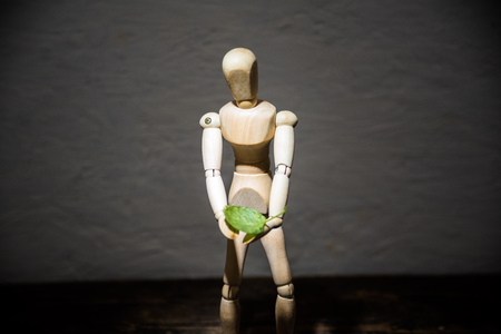 wooden toy in the image of a man on a dark background in hands with a green leafの写真素材