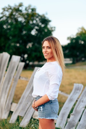Young beautiful blonde in a white shirt and short denim shorts outdoorsの写真素材