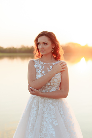 young beautiful bride in white dress on wooden pier near water at sunset 1の写真素材