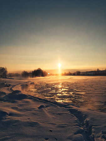winter frosty sunset over the frozen snow-covered riverの写真素材