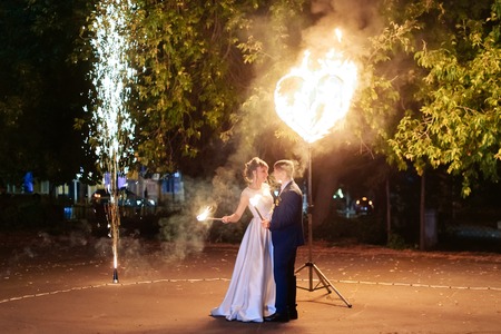 beautiful young newlywed couple with fire torches in their hands and fireworksの写真素材