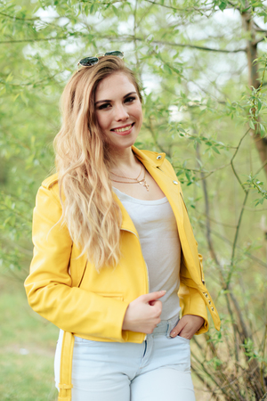 beautiful blonde girl in a yellow jacket on the background of nature outdoorsの写真素材