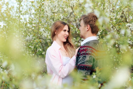 a young couple in love cuddles against the background of blooming spring cherry orchardsの写真素材