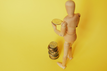 wooden man on a yellow background with coinsの写真素材