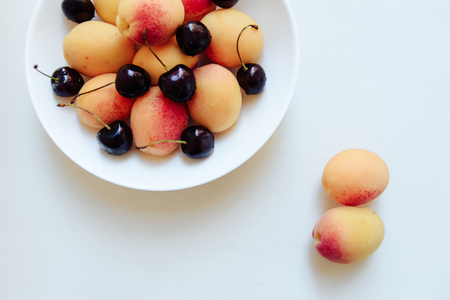 apricots and cherry in a plate on a light backgroundの写真素材