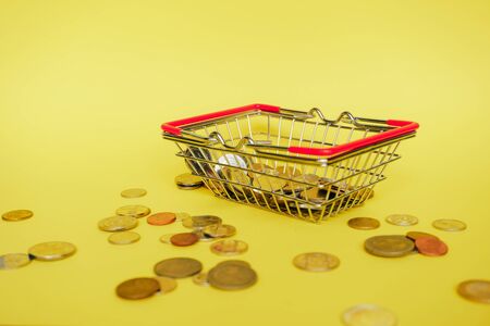 miniature shopping cart on a yellow background filled with coins