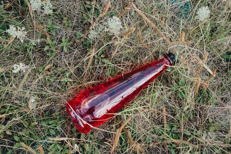 a bottle of red lemonade lies on the withered grassの写真素材