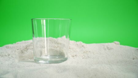 glass with ice and soda water and lemon on the sand on a green background