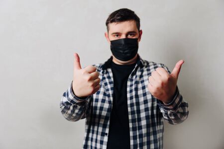 a man in a black medical mask on a gray background gives a thumbs up 1の写真素材