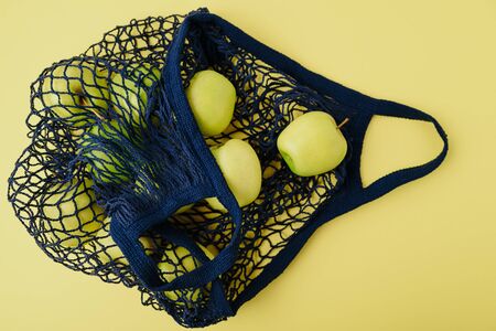 blue string bag with green apples on a yellow backgroundの写真素材