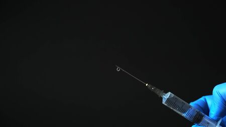 Medical syringe in hand in a blue glove on a black backgroundの写真素材