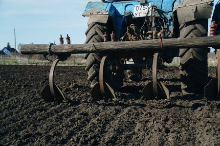 The tractor cultivates and cuts furrows in the field. Tractor work in the black soil field in the villageの写真素材