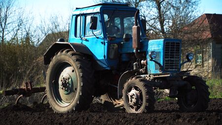 The tractor cultivates and cuts furrows in the field. Tractor work in the black soil field in the villageの写真素材