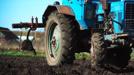 The tractor cultivates and cuts furrows in the field. Tractor work in the black soil field in the villageの写真素材