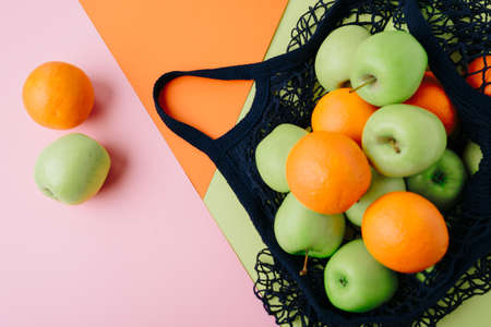 apples and oranges in a blue string bag on a colored background. Fruits in a grid on multicolored backgroundsの写真素材