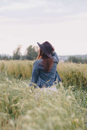Beautiful young girl in a denim jacket in a green field of rye at sunsetの写真素材