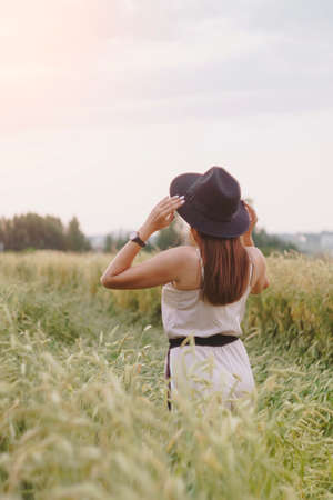 A girl in a white dress and a black hat in a field of ryeの写真素材