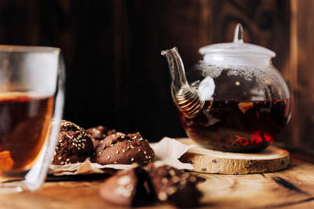 Teapot with black tea and homemade chocolate cookies on a brown natural wooden backgroundの写真素材