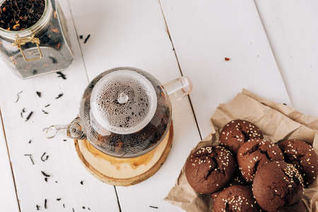Teapot with black tea and homemade chocolate cookies on a white natural wooden background