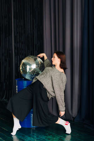 Beautiful young woman in gray sweater and disco ball at home