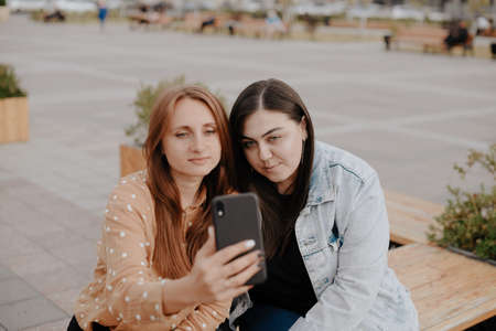 Two young women sit in a city Park with a phoneの写真素材