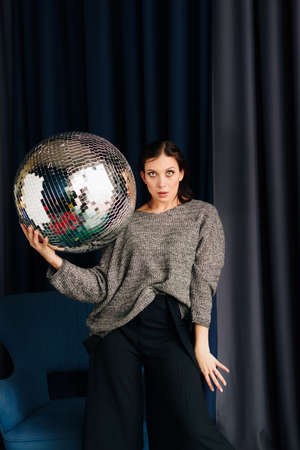 Beautiful young woman in gray sweater and disco ball at homeの写真素材