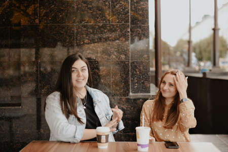 Two young women sit in an open cafe in the city