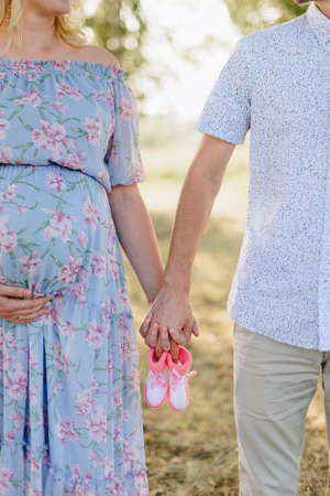Pregnant girl with her husband holding hands in nature in the fieldの写真素材